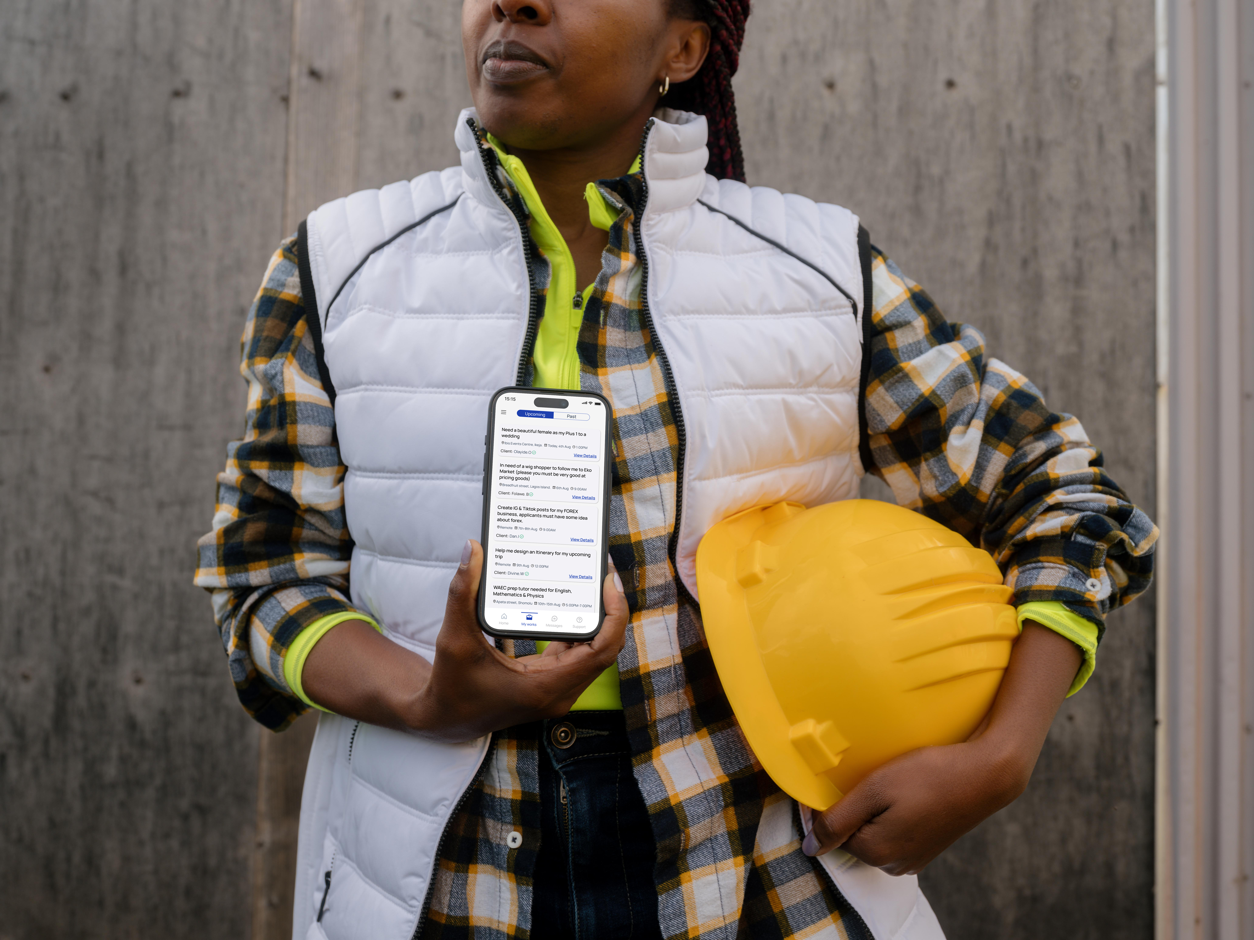 A construction worker in a hard hat holding a phone running the Hustle app while browsing available gig listings